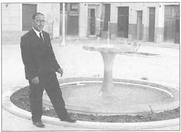 Año 1960. Vista de la Plaça de Baix con la desaparecida fuente. Al fondo puede distinguirse el letrero anunciador de la fontanería Félix. En la foto, Joaquín "El Sacristán".